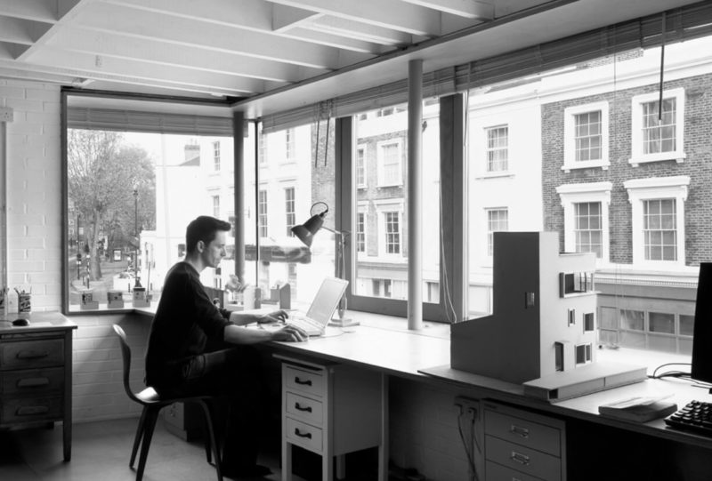 Man sitting at desk near large windows in a studio overlooking a street